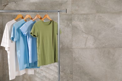 Photo of Clean T-shirts hanging on rack near gray marble wall. Space for text