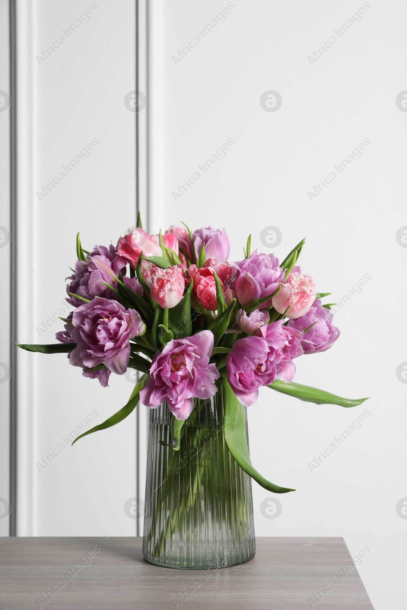 Photo of Beautiful bouquet of colorful tulip flowers in vase on wooden table
