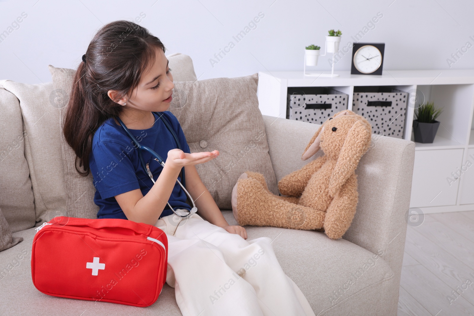 Photo of Little girl playing doctor with toy bunny on sofa indoors. Pediatrician practice