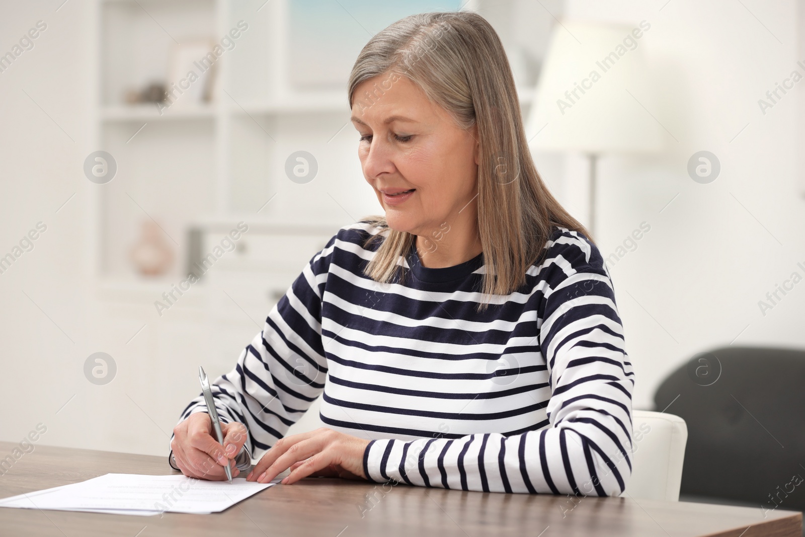 Photo of Senior woman signing Last Will and Testament at wooden table indoors