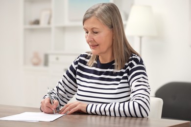 Senior woman signing Last Will and Testament at wooden table indoors