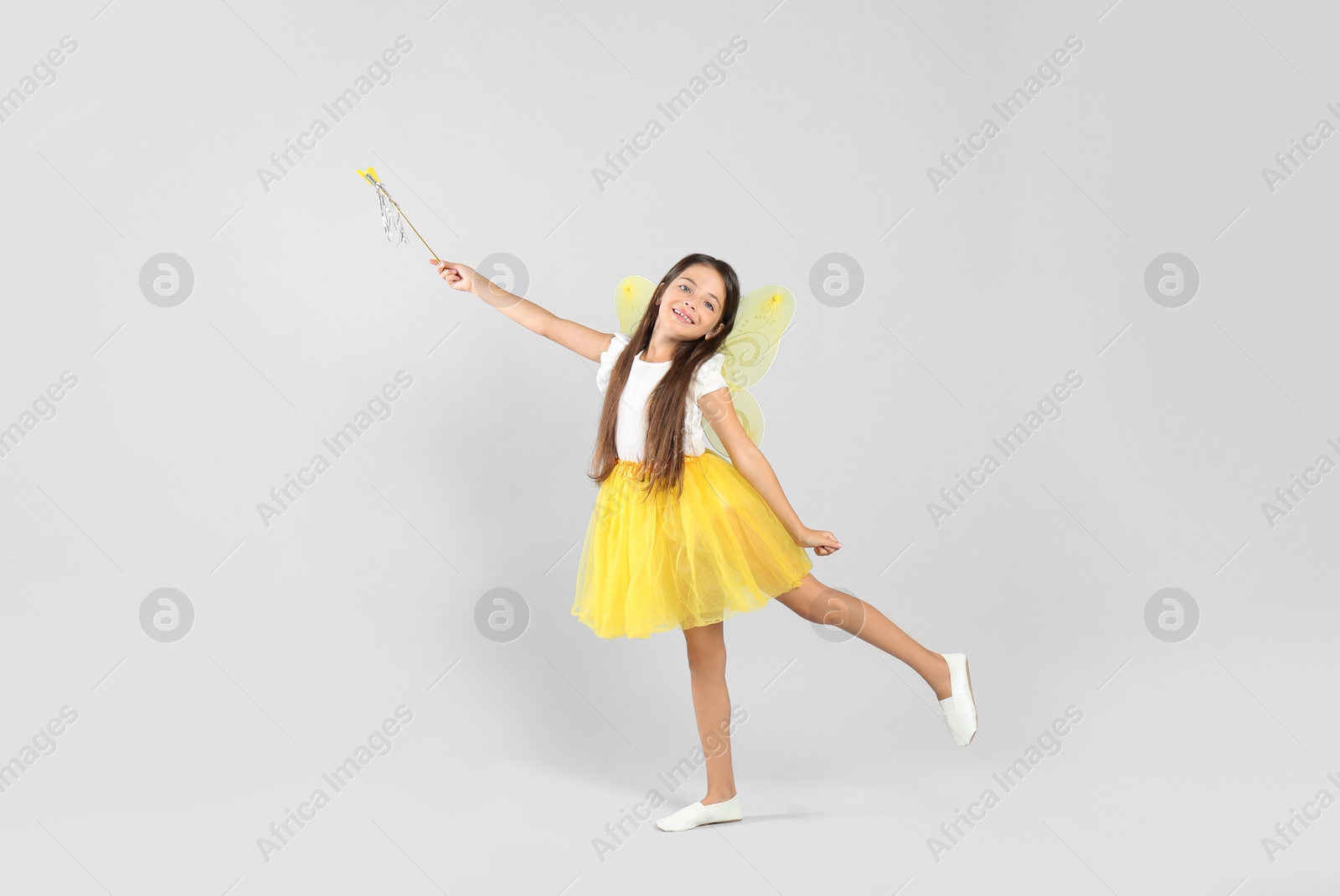 Photo of Cute little girl in fairy costume with yellow wings and magic wand on light background