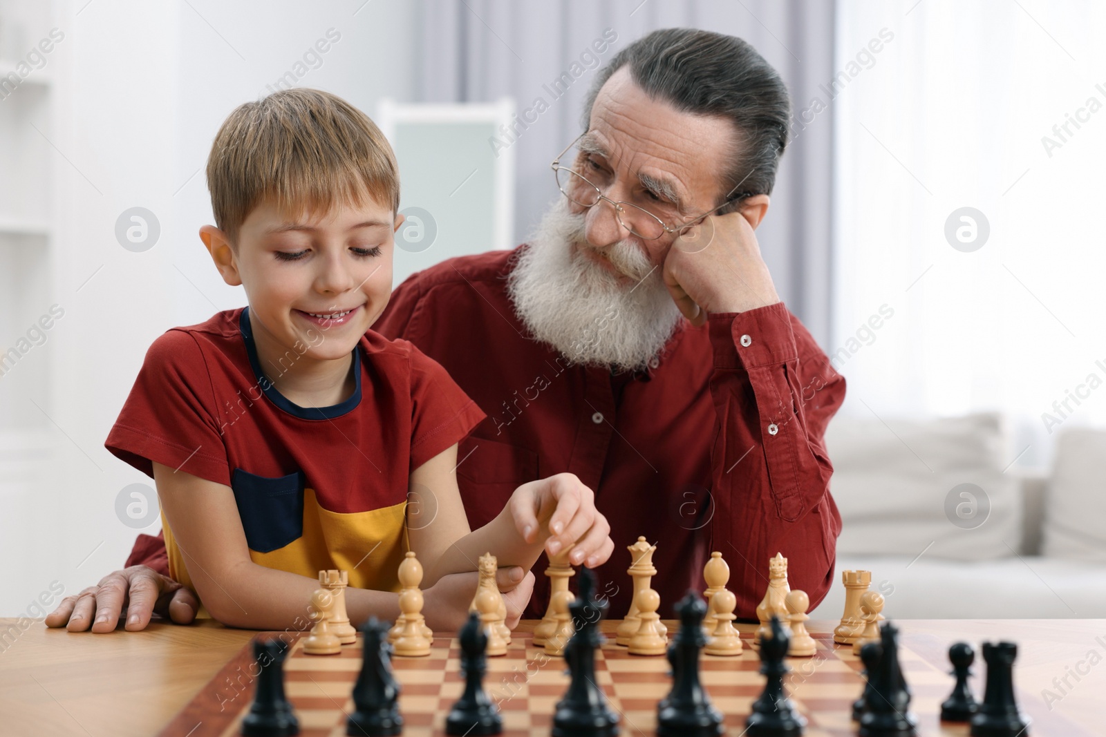 Photo of Senior man teaching his grandson to play chess at home