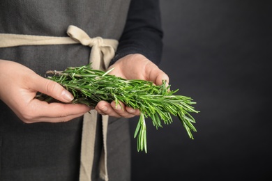 Photo of Young woman holding bunch of fresh rosemary on black background, closeup