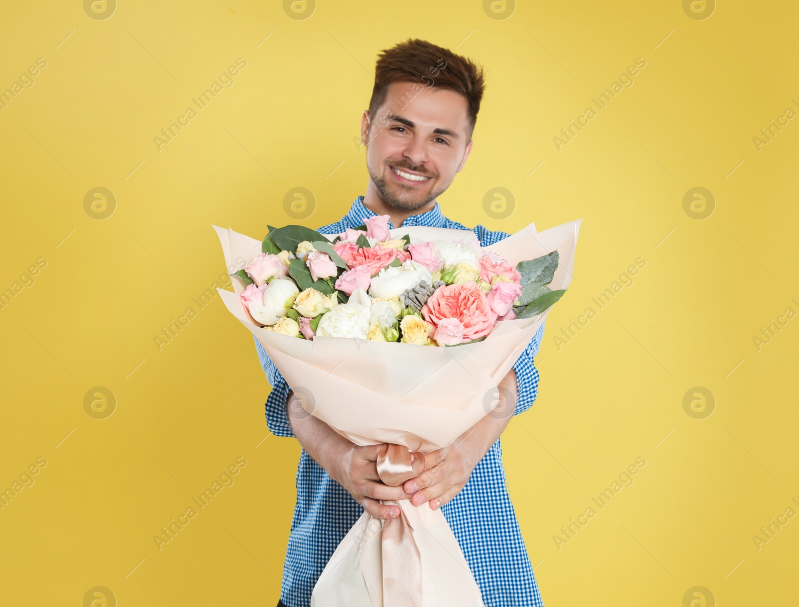 Photo of Young handsome man with beautiful flower bouquet on yellow background