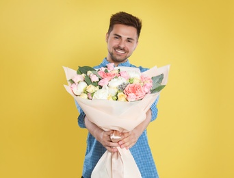 Photo of Young handsome man with beautiful flower bouquet on yellow background