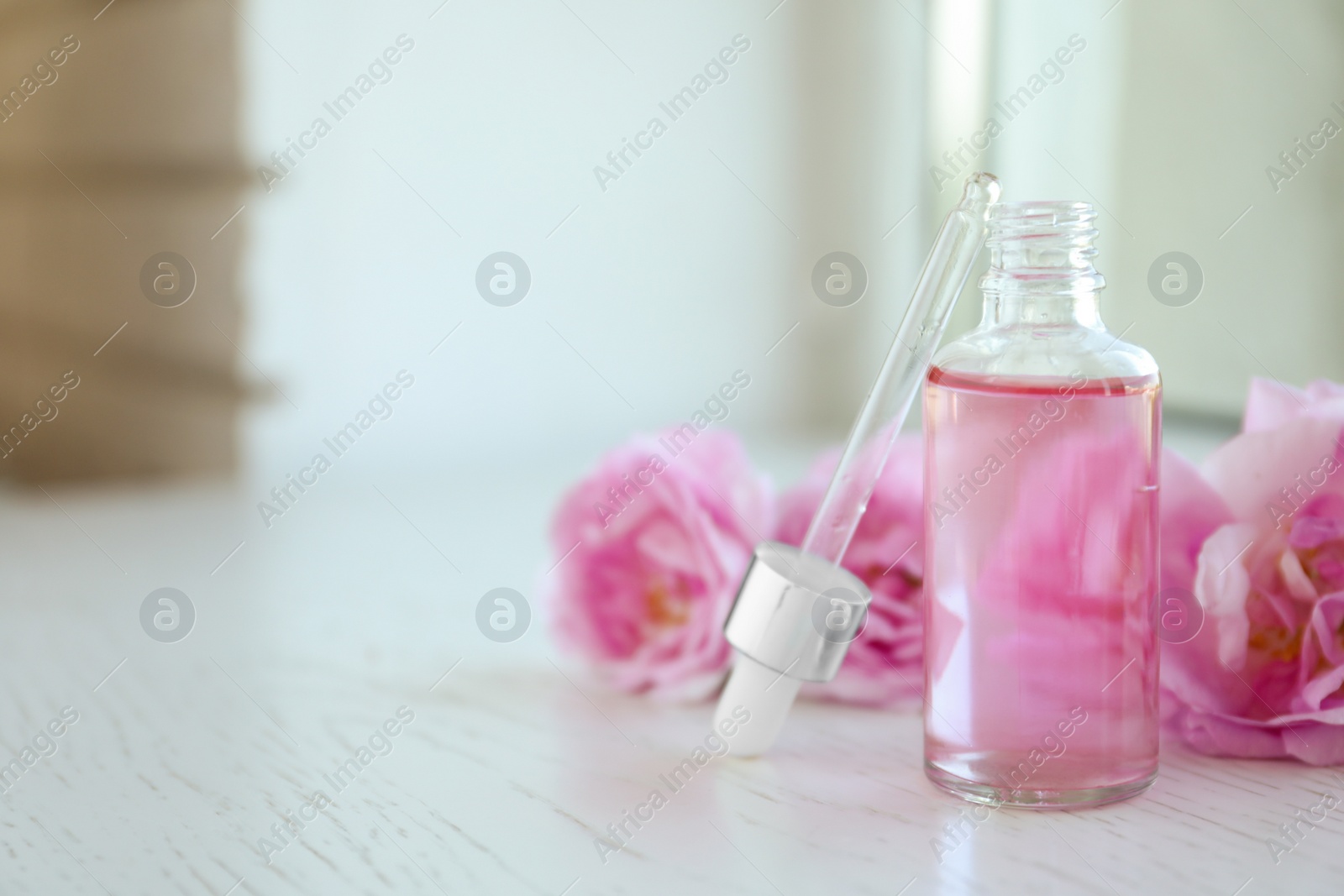 Photo of Bottle of rose essential oil, pipette and fresh flowers on window sill, space for text