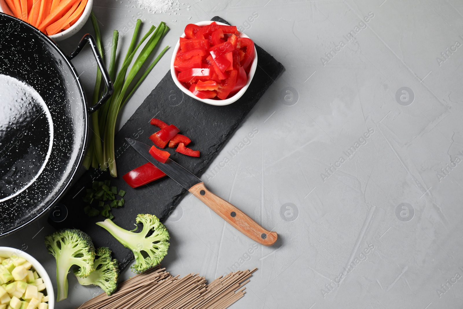 Photo of Wok pan, noodles and other products on light grey table, flat lay. Space for text