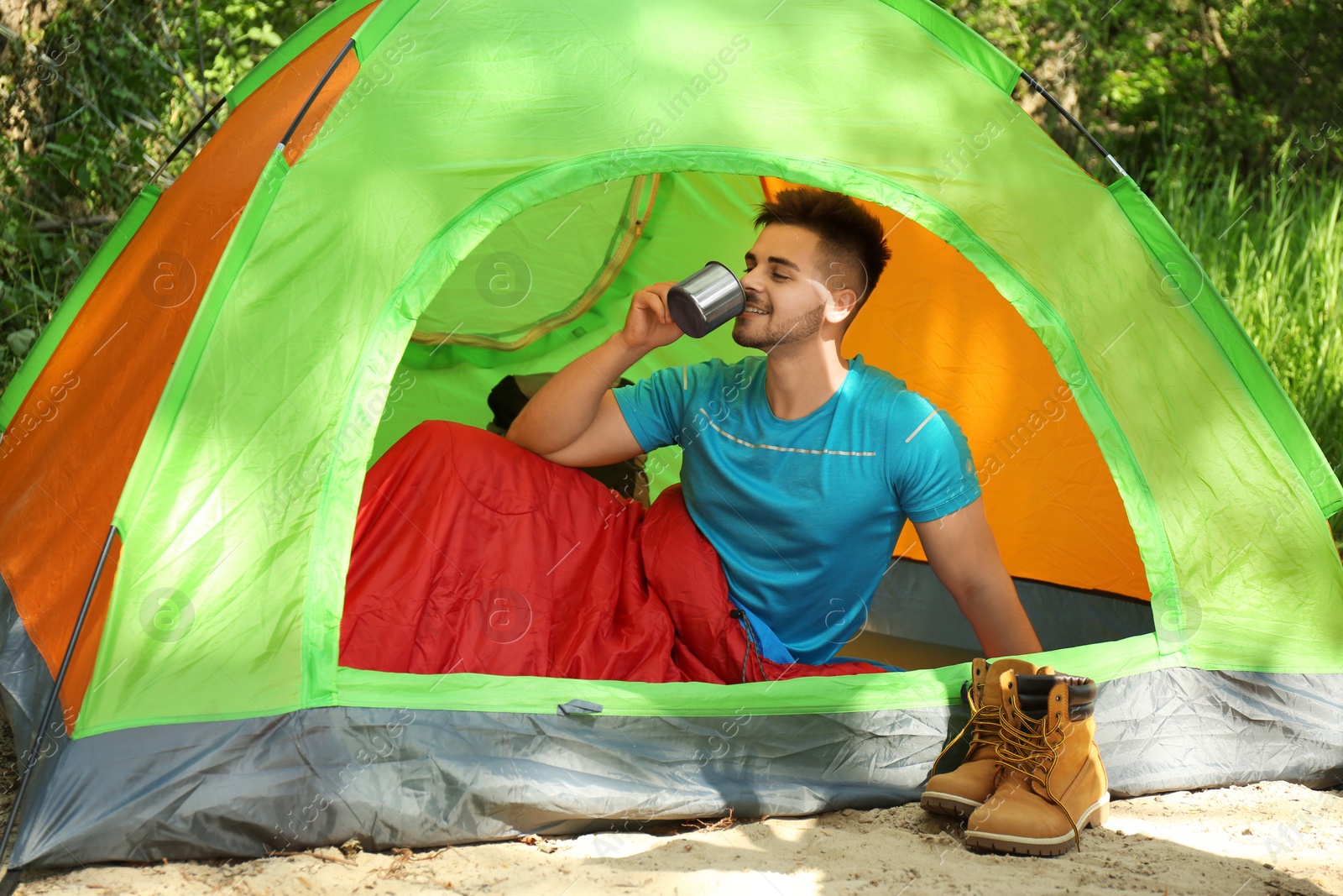 Photo of Young man drinking in sleeping bag inside tent