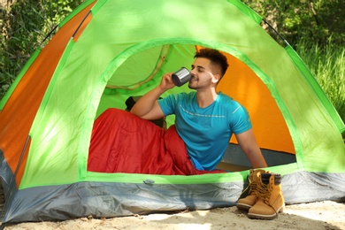 Photo of Young man drinking in sleeping bag inside tent