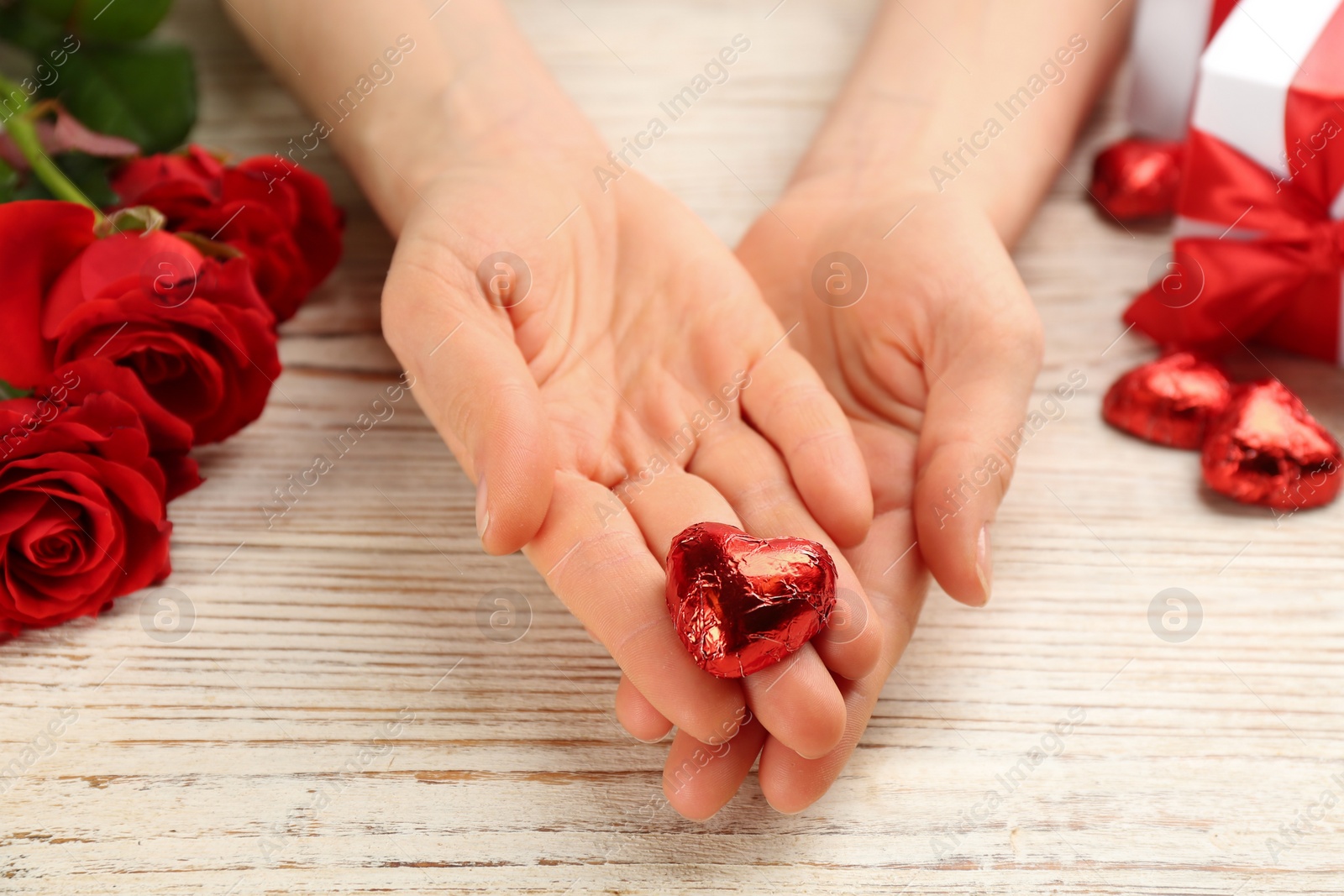 Photo of Woman holding heart shaped chocolate candy at white wooden table, closeup