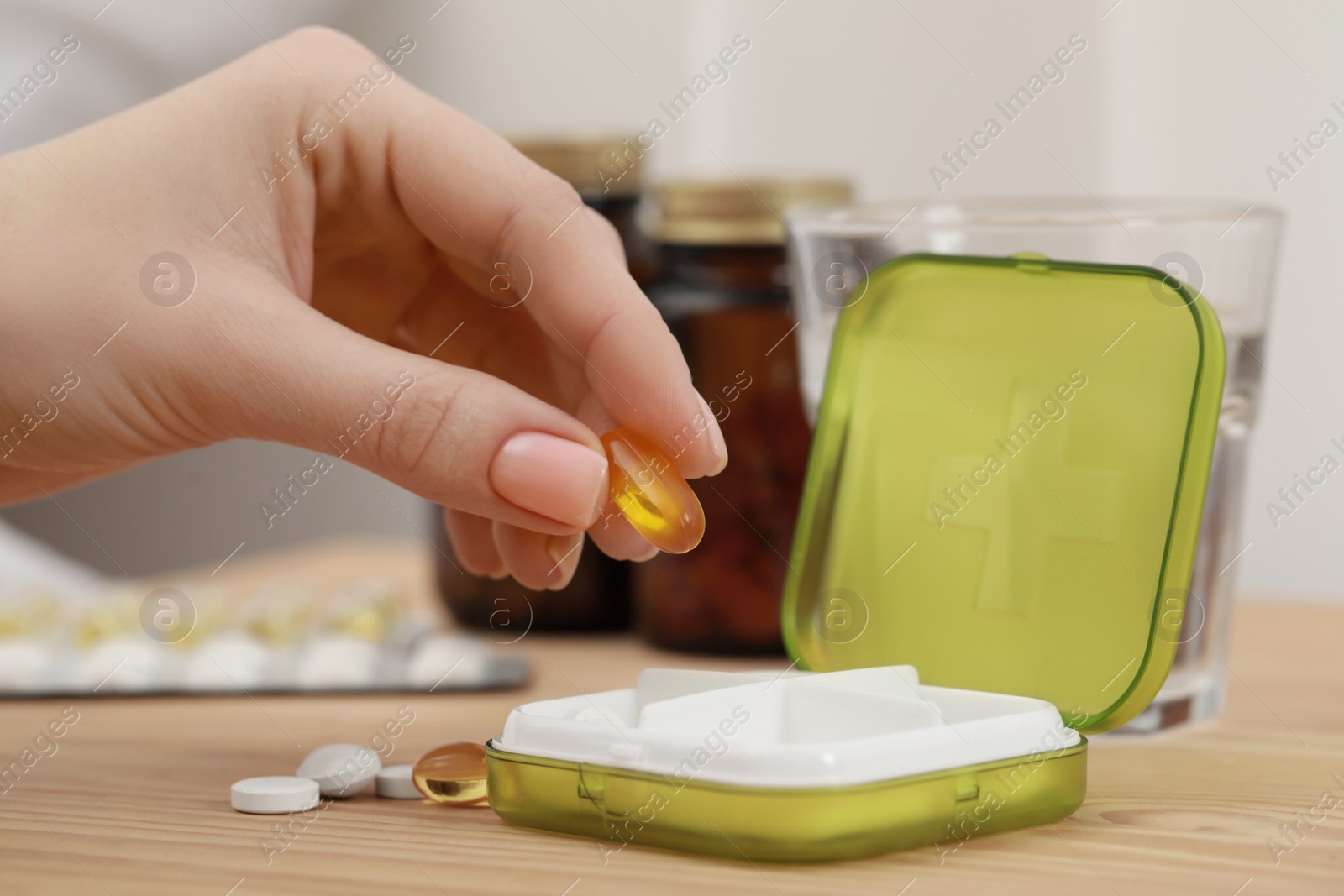 Photo of Woman taking pill from plastic box at wooden table, closeup