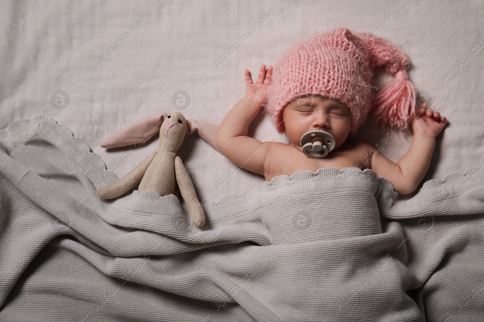 Photo of Cute newborn baby in warm hat sleeping on light bedsheet, top view 