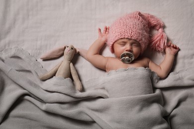 Photo of Cute newborn baby in warm hat sleeping on light bedsheet, top view 