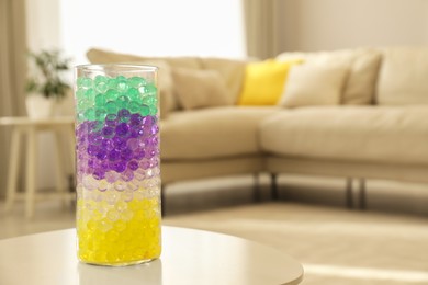 Photo of Different color fillers in glass vase on white table at home, space for text. Water beads