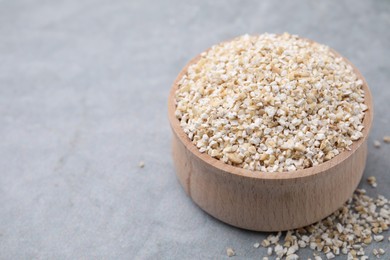Photo of Raw barley groats in bowl on grey table, closeup. Space for text