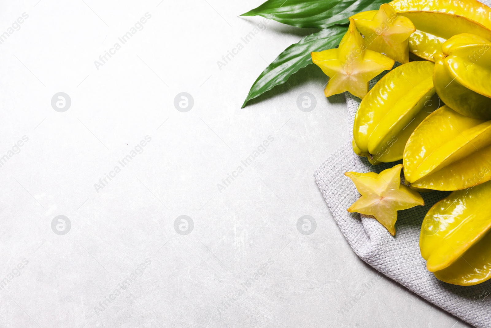 Photo of Cut and whole carambolas with green leaves on light table, above view. Space for text