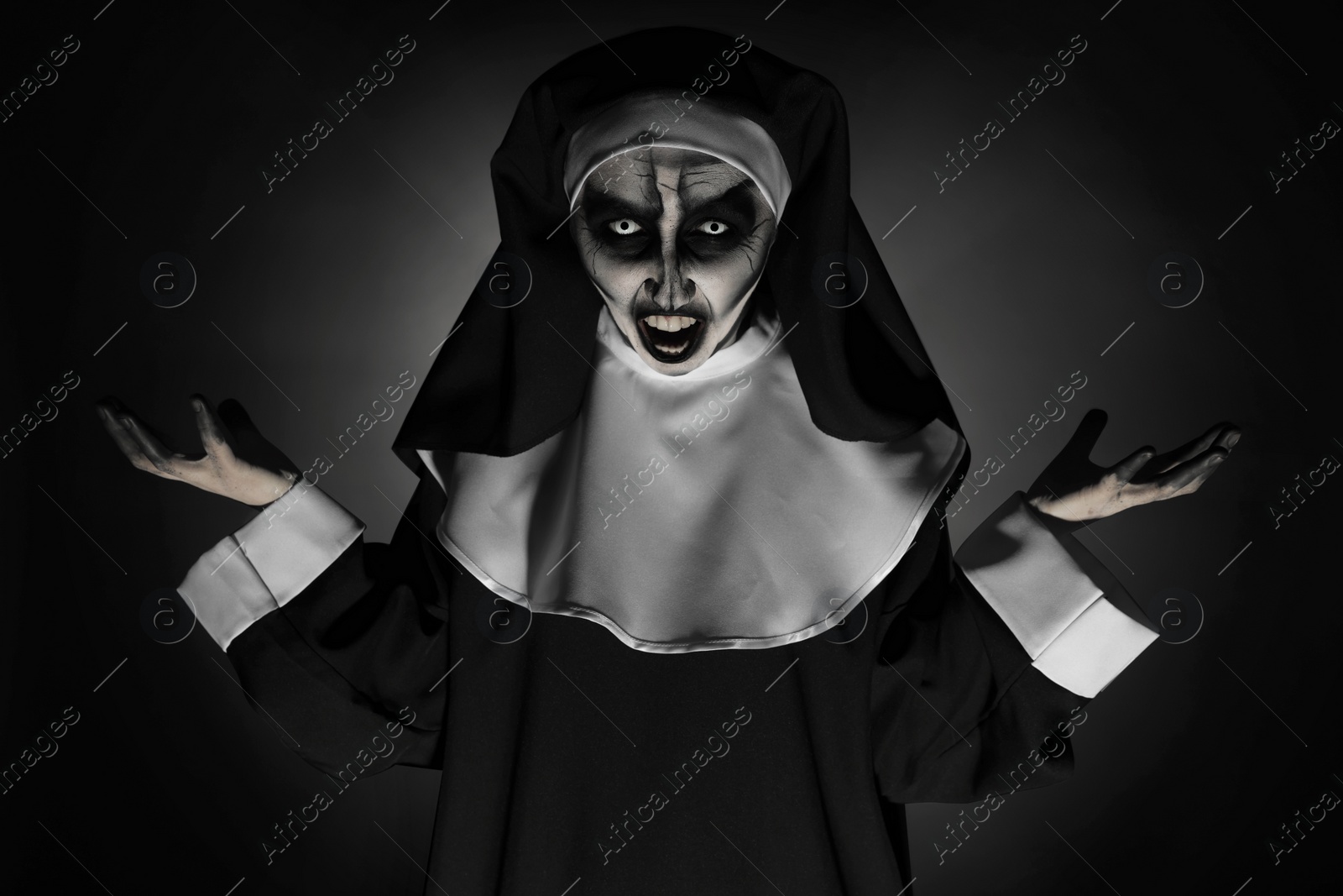 Photo of Portrait of scary devilish nun on black background. Halloween party look