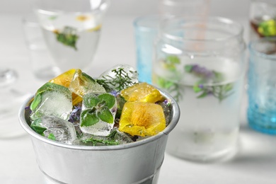 Bucket of ice cubes with flowers on blurred background, closeup