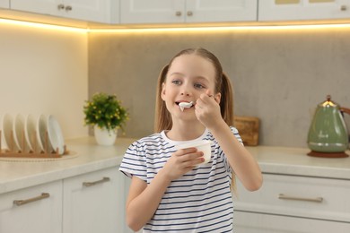 Photo of Cute little girl eating tasty yogurt in kitchen