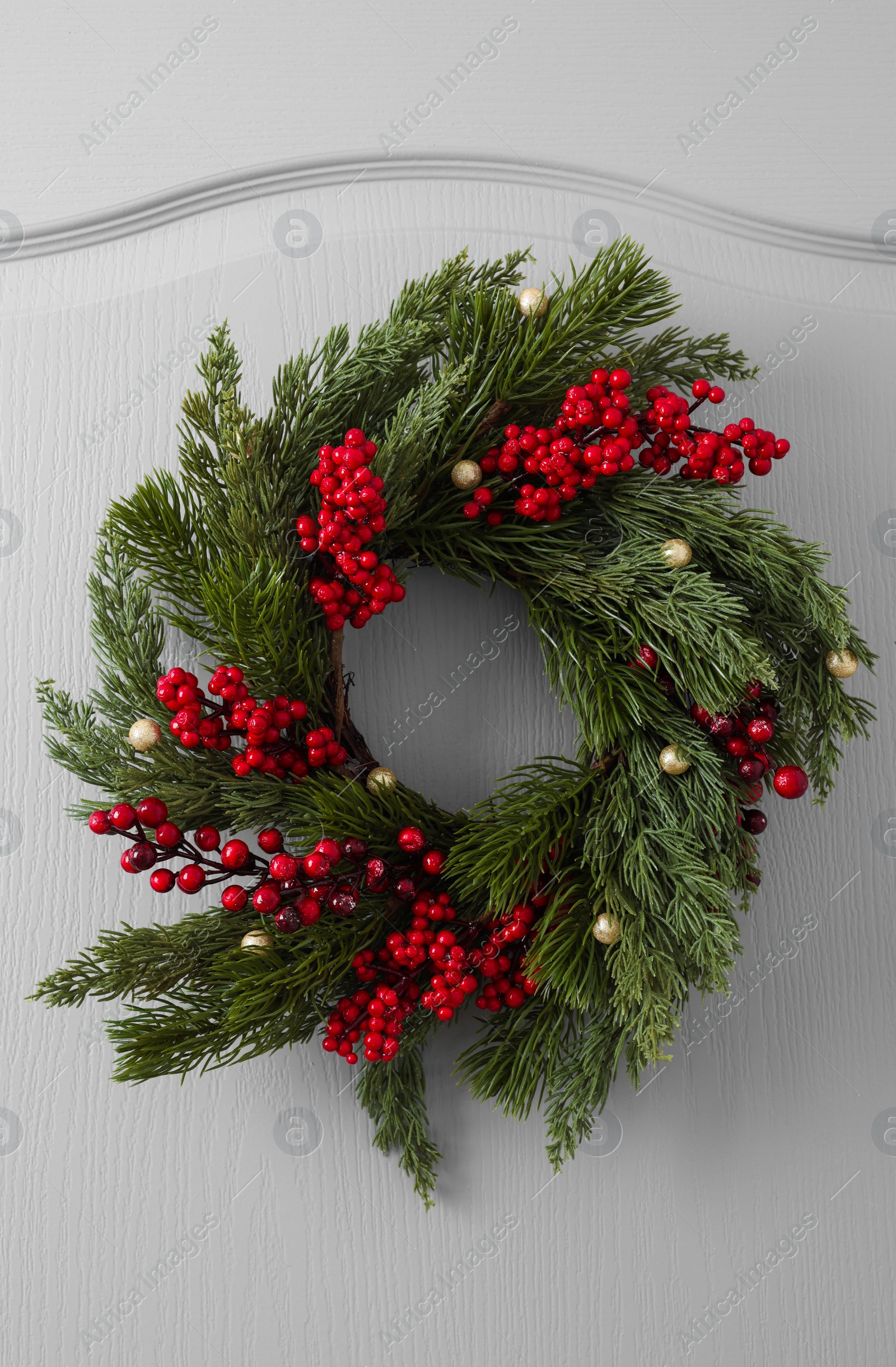 Photo of Beautiful Christmas wreath with red berries and decor hanging on white door