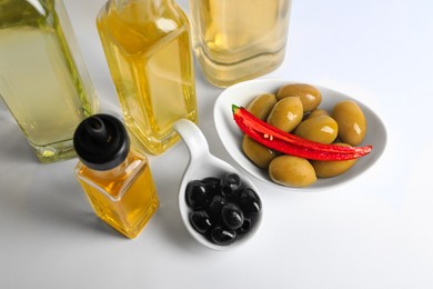 Photo of Bottles of different cooking oils and olives on white background, above view