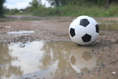 Photo of Soccer ball near puddle outdoors, space for text