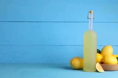 Photo of Bottle of tasty limoncello liqueur and lemons on light blue table, space for text