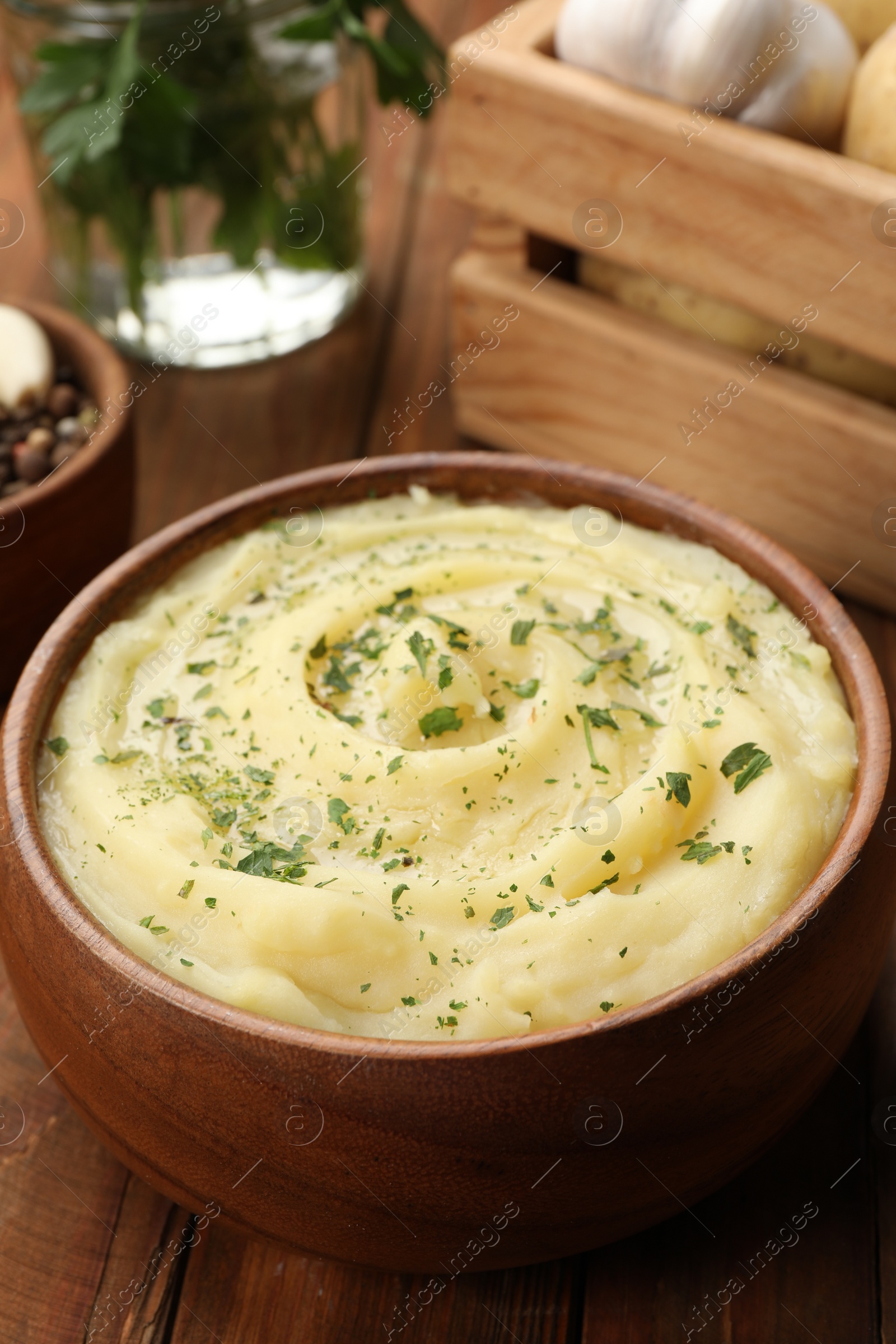 Photo of Bowl of tasty mashed potato with greens, garlic and pepper on wooden table, closeup