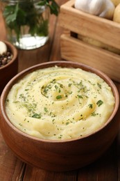 Bowl of tasty mashed potato with greens, garlic and pepper on wooden table, closeup