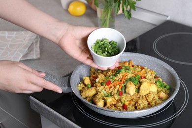 Photo of Woman adding cut green onion to rice with meat and vegetables in frying pan, closeup