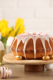 Photo of Delicious Easter cake decorated with sprinkles near eggs on wooden table