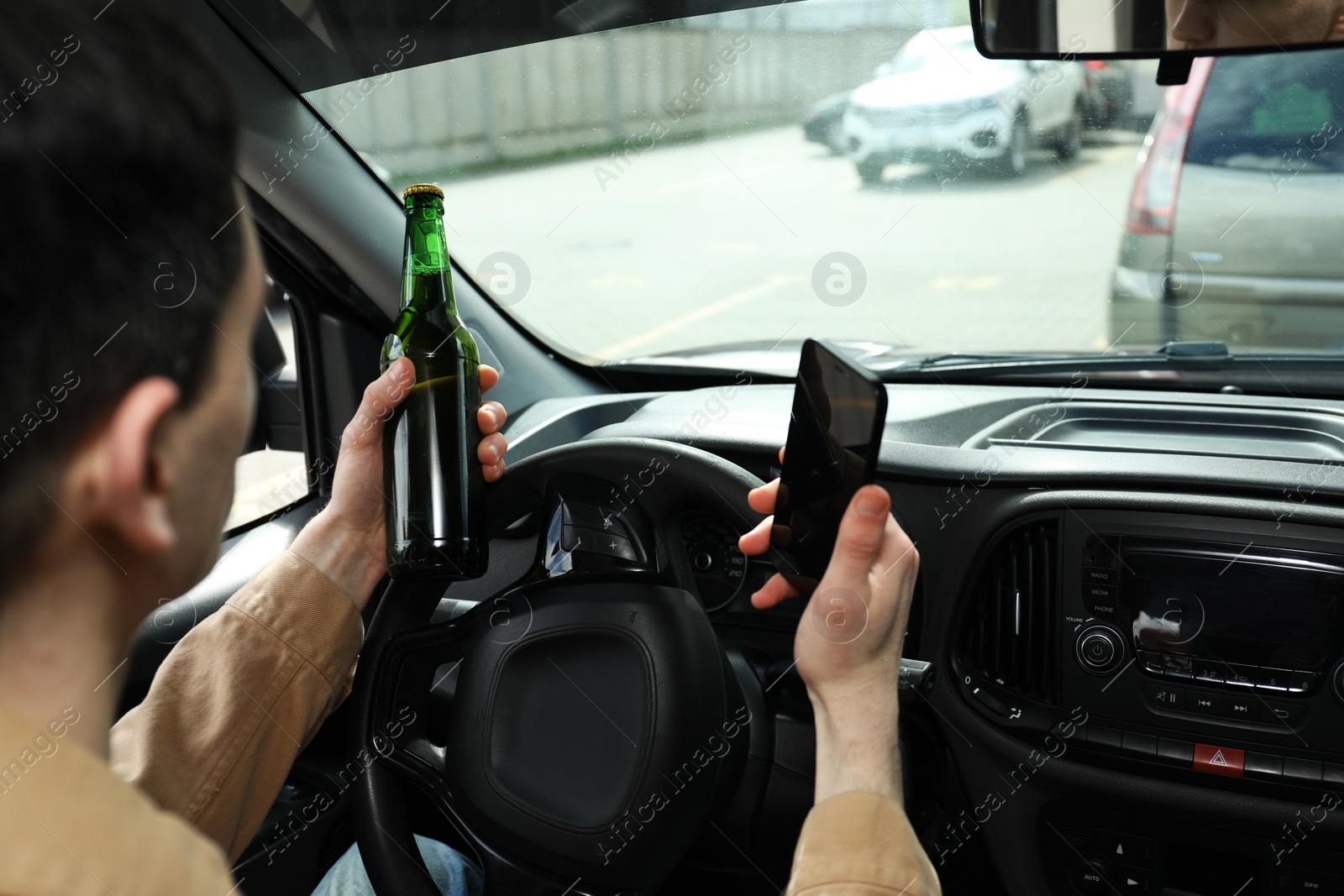 Photo of Man with bottle of beer and smartphone in car, closeup. Don't drink and drive concept