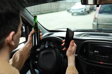 Photo of Man with bottle of beer and smartphone in car, closeup. Don't drink and drive concept