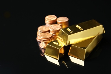 Shiny gold bars and coins on black background