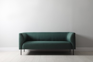 Photo of Comfortable green sofa near white wall indoors. Interior design