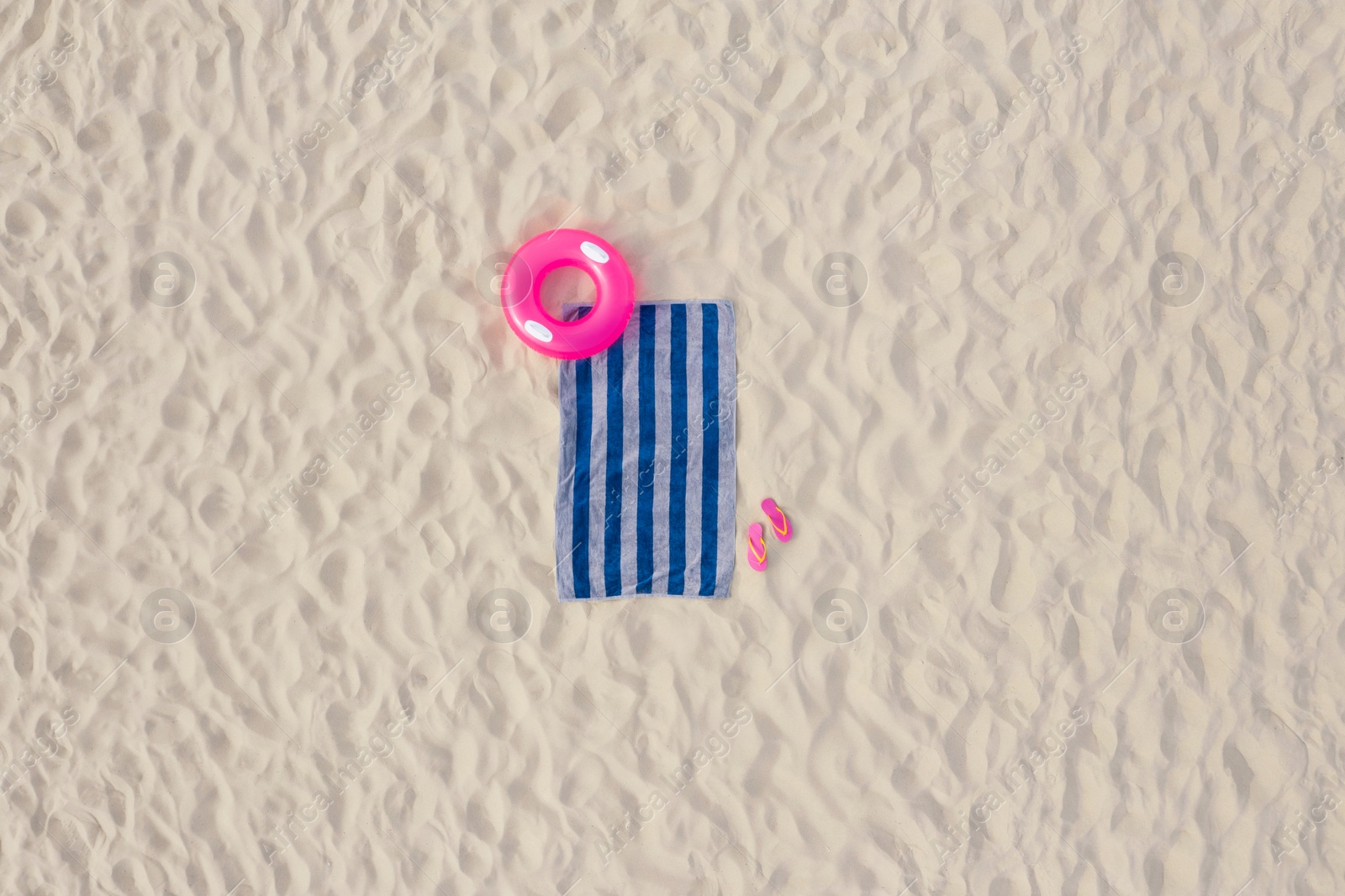 Image of Striped beach towel, flip flops and swim ring on sand, aerial view