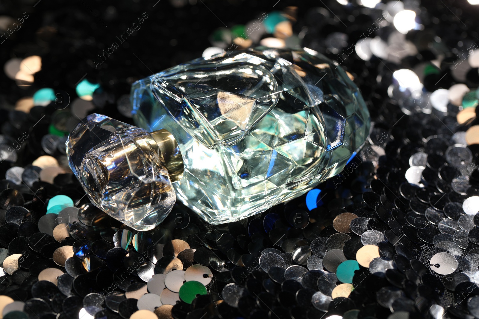 Photo of Luxury perfume in bottle on fabric with shiny sequins, closeup