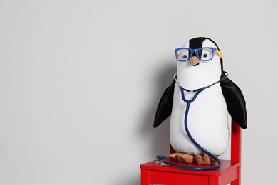 Photo of Toy penguin with eyeglasses and stethoscope on white background, space for text. Pediatrician practice