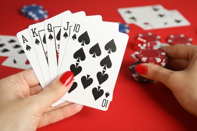 Photo of Woman holding playing cards with royal flush combination and poker chips at red table, closeup