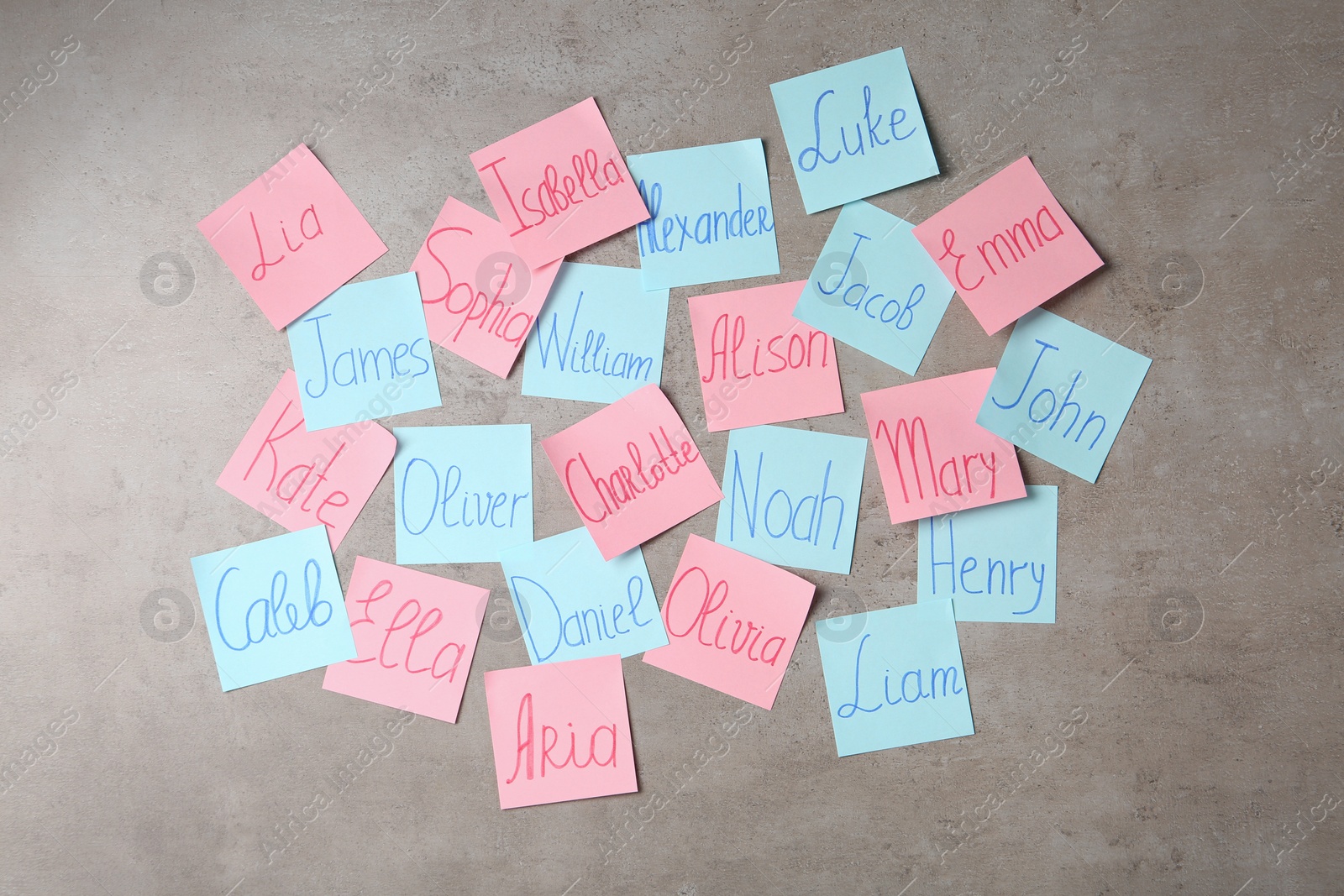 Photo of Colorful paper sheets with written different baby names on grey background, flat lay