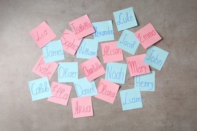 Colorful paper sheets with written different baby names on grey background, flat lay