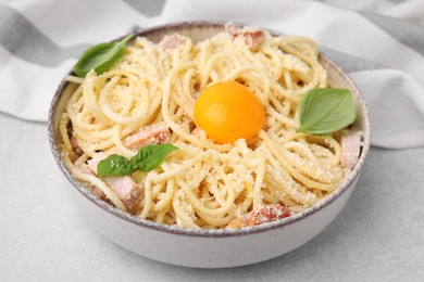 Photo of Bowl of tasty pasta Carbonara with basil leaves and egg yolk on light grey table