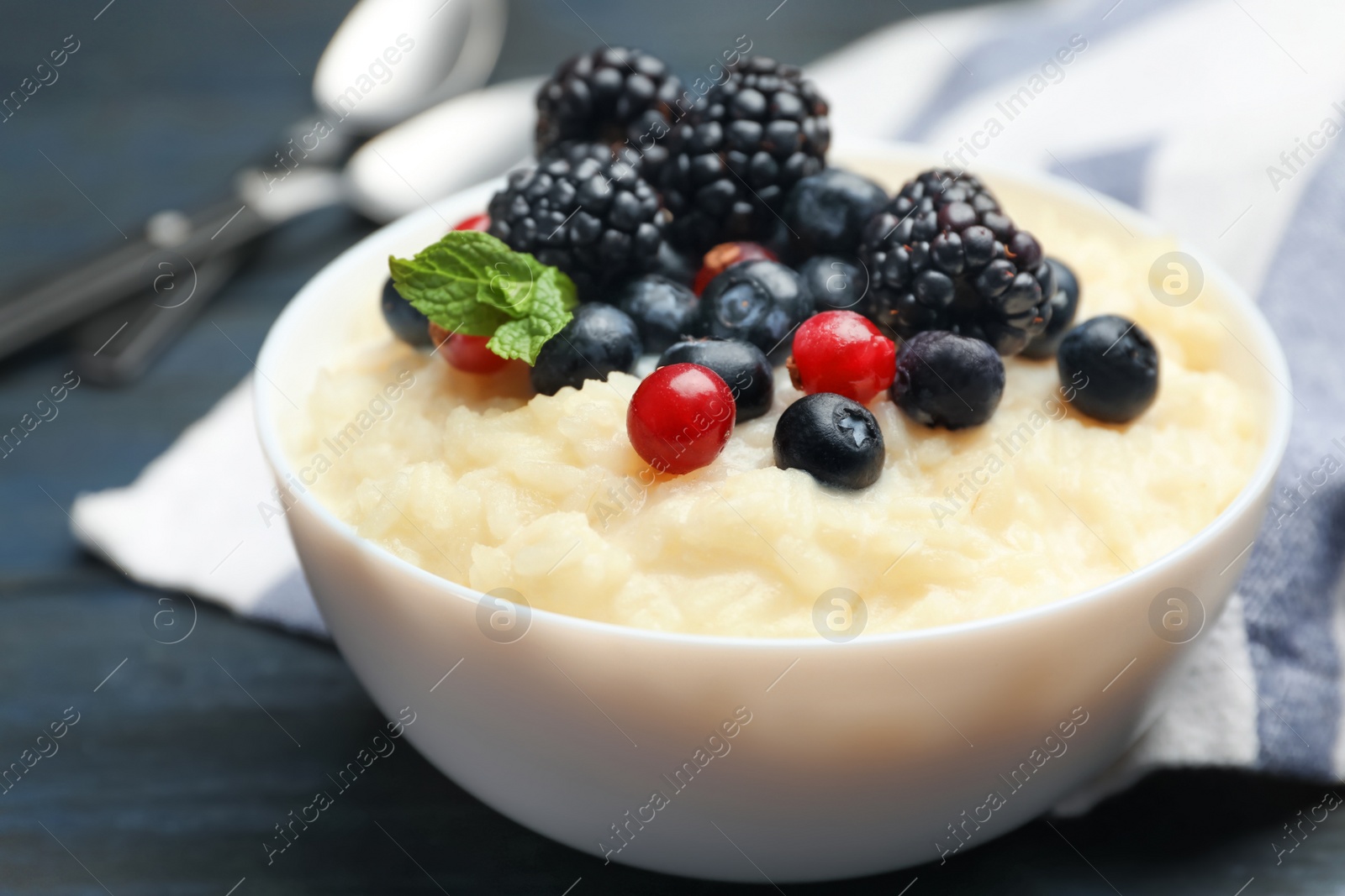 Photo of Delicious rice pudding with berries on dark wooden table, closeup