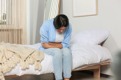 Photo of Young woman suffering from cystitis on bed at home