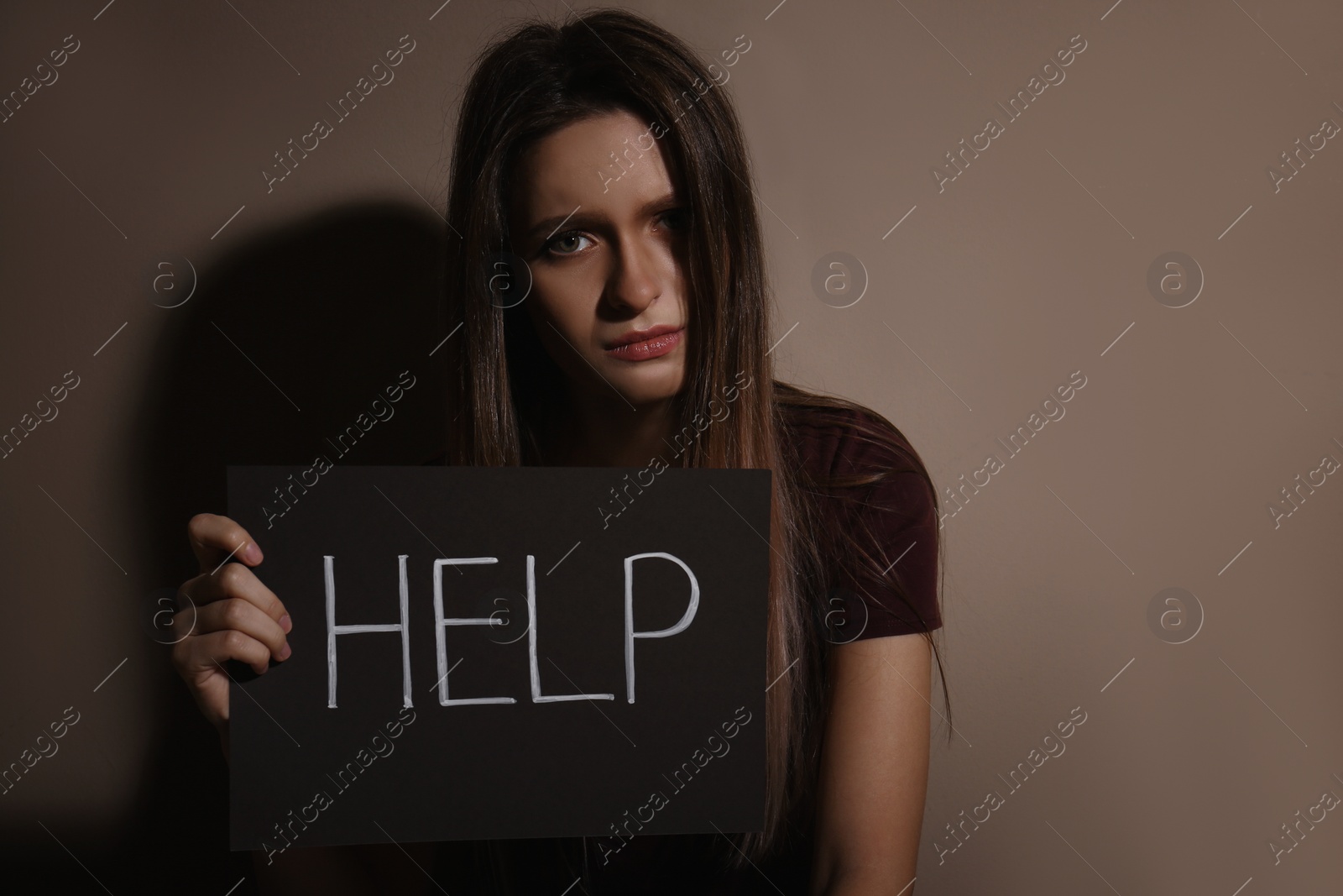 Photo of Abused young woman with sign HELP near beige wall. Domestic violence concept