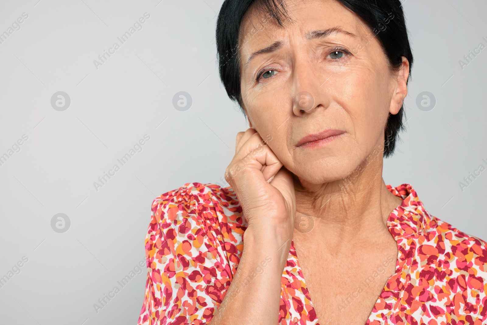 Photo of Senior woman suffering from ear pain on light grey background, closeup. Space for text