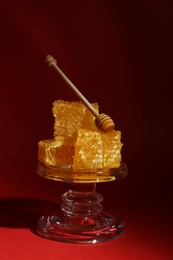 Natural honeycombs and wooden dipper on glass stand against burgundy background