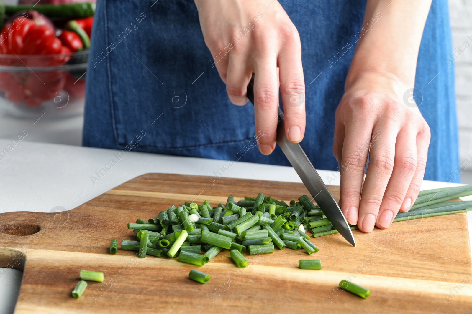 Photo of Woman cutting green spring onion on wooden board at white table, closeup