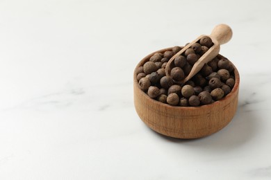 Photo of Dry allspice berries (Jamaica pepper) in bowl and scoop on white marble table, space for text